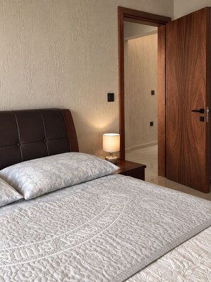A bedroom with a bed, a nightstand, a lamp, and a wooden wardrobe. - Tranquil 2-bedroom apartment in delightful Mindelo perfect for relaxing (Mindelo)