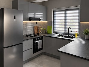 A modern kitchen with stainless steel appliances, a built-in oven, and a window with blinds. - Tranquil 2-bedroom apartment in delightful Mindelo perfect for relaxing (Mindelo)