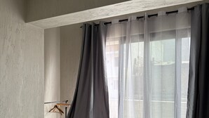 Un dormitori amb un llit gran, una finestra amb cortines i una perxa de fusta a la paret.