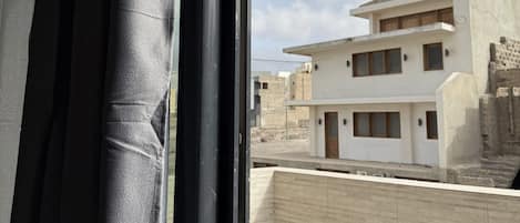 A view through a window with a curtain, revealing a modern building with multiple floors and a balcony.