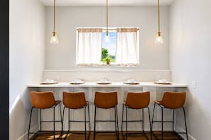 A kitchen with a long counter, five bar stools, and a window with curtains.