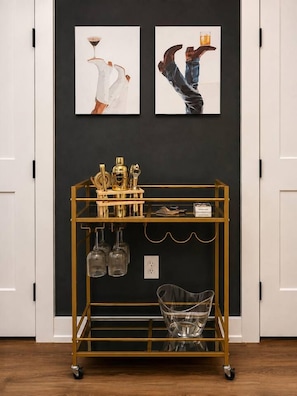 A room with a gold-colored cart holding various items, a black wall with two framed artworks, and a white door.