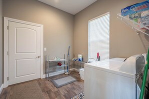 A laundry room with a washing machine, shelves with cleaning supplies, a mop, and a door. - Sanabell Lookout - REDHEAD COVE!!! (Osage Beach)