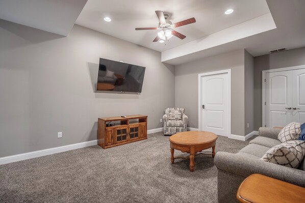 A living room with a ceiling fan, a flat-screen TV, a wooden entertainment center, a patterned armchair, and a gray sofa. - Sanabell Lookout - REDHEAD COVE!!! (Osage Beach)