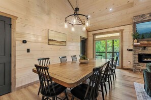 A wooden dining room with a large table and chairs, a chandelier, and a stone fireplace. - New | Mtn Views & Modern Luxury | Sleeps 12 | 5 Fireplaces | Pool & Hot Tub (Sevierville)