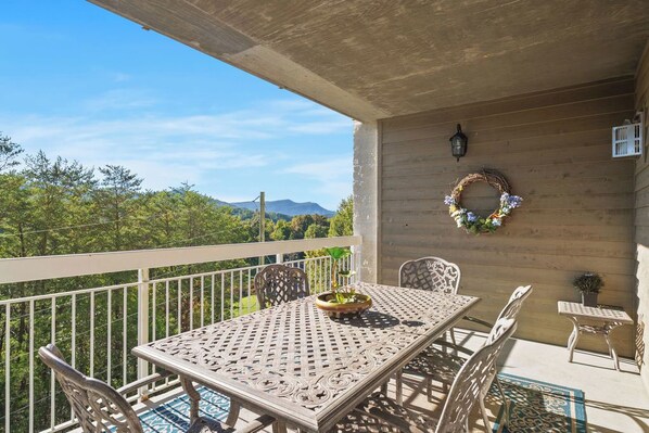 A balcony with a table and chairs, a decorative wreath, and a view of trees and mountains. - Whispering Pines 634 | 4BR Luxury Condo in the Heart of Pigeon Forge Sleeps 10 (Pigeon Forge)