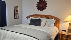 Ein ordentlich bezogenes Bett mit einer gemusterten Tagesdecke, einem hölzernen Kopfteil und einem Nachttisch mit Lampe und Radio.