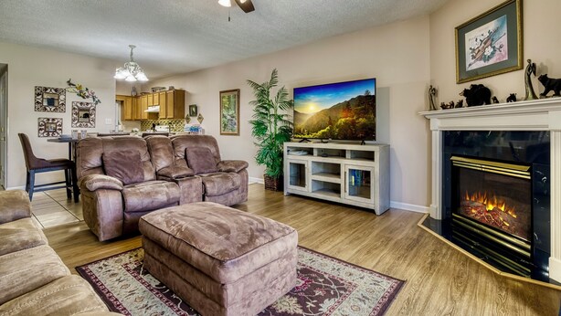 Una sala de estar con sofá, reposapiés, televisión, chimenea y ventilador de techo.