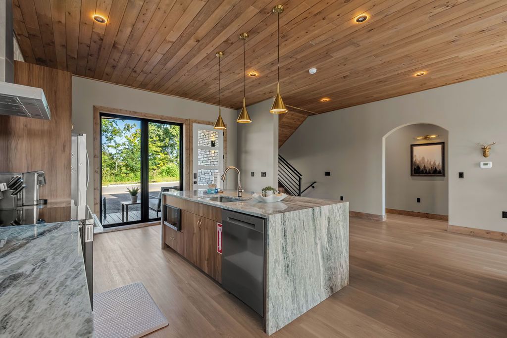 A modern kitchen with a marble island, wooden ceiling, and pendant lighting.