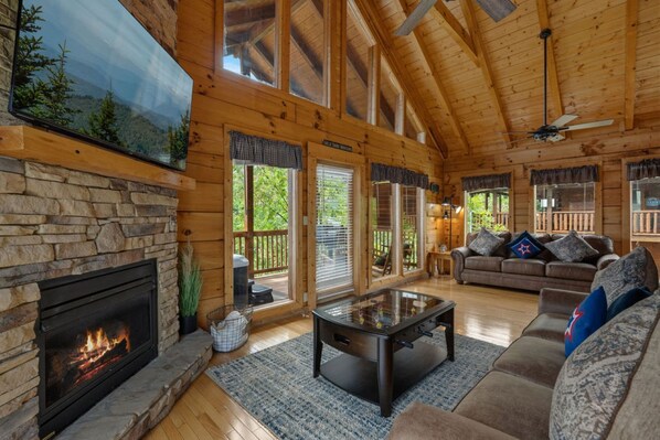 A log cabin interior with a stone fireplace, a leather sofa, and a ceiling fan. - Smoky's Retreat Pigeon Forge | Hot Tub | Arcade (Pigeon Forge)