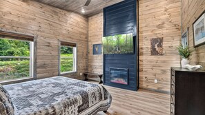 Un dormitorio con cama, chimenea, paredes de madera y ventana con vistas a zonas verdes.