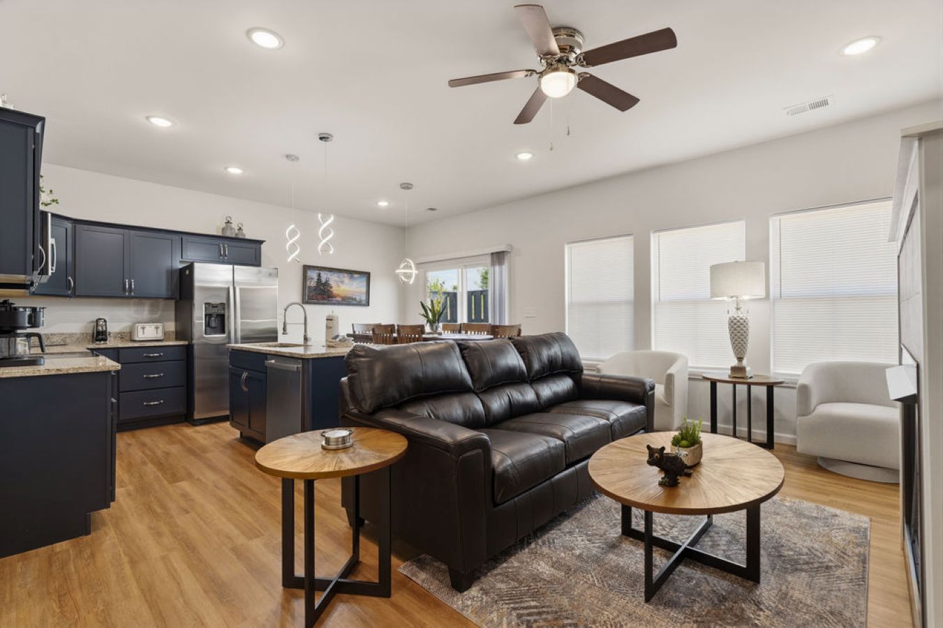 A modern living room with a leather sofa, two coffee tables, and a dining area with a kitchen in the background.