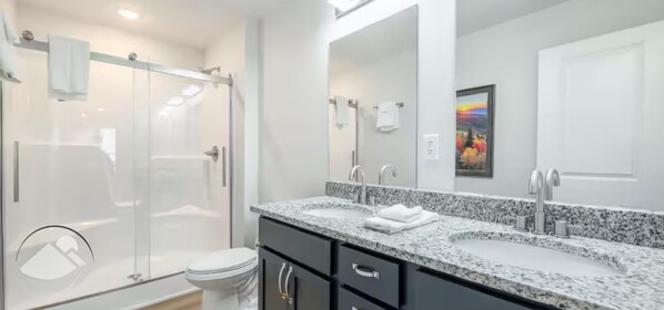 Un baño moderno con ducha envuelta en vidrio, tocador doble y un espejo grande.