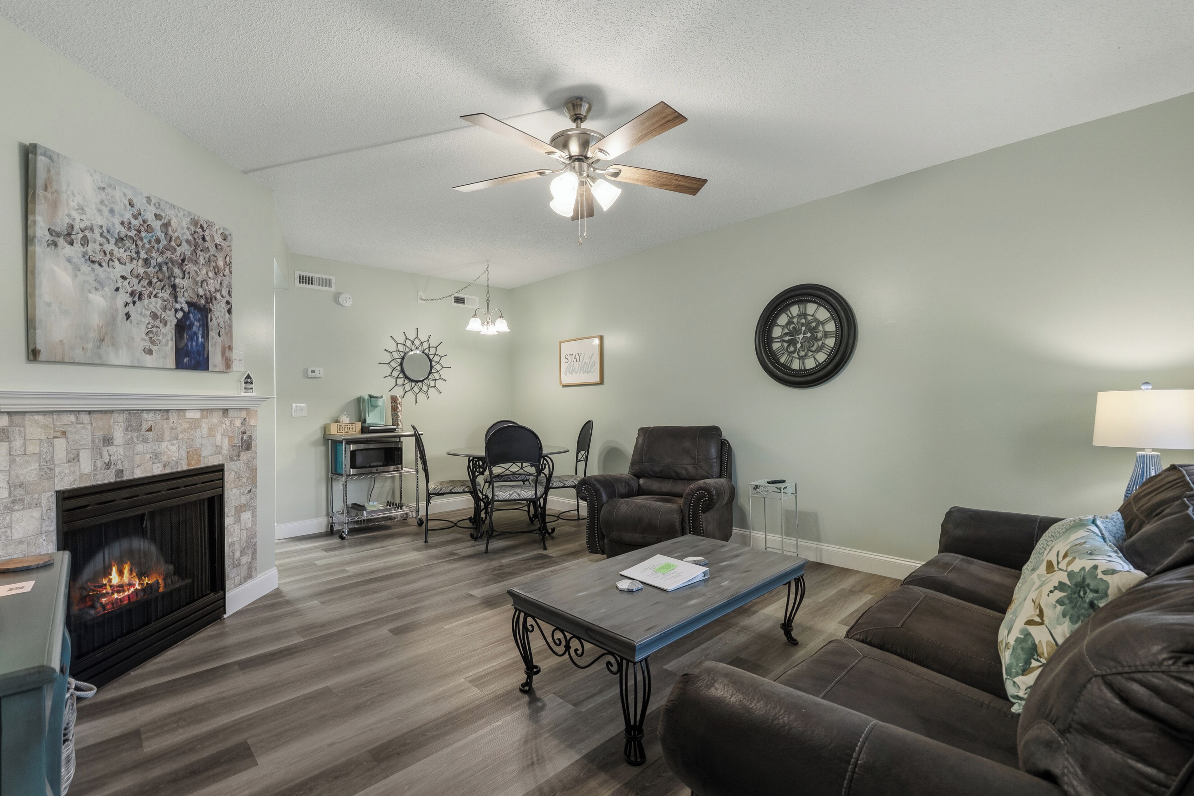 A living room with a fireplace, a ceiling fan, a clock, and a coffee table.