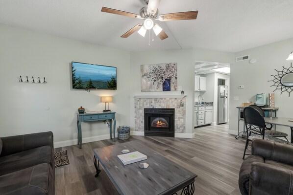 A living room with a fireplace, a television, and a ceiling fan. - Downtown Pigeon Forge Condo| One bedroom, one bathroom| Near The Island (Pigeon Forge)