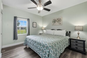 A bedroom with a bed, a nightstand, a lamp, a ceiling fan, a window with curtains, and a wall with a framed picture. - Downtown Pigeon Forge Condo| One bedroom, one bathroom| Near The Island (Pigeon Forge)