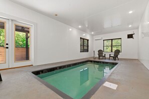 Ein Schwimmbecken mit gefliestem Sonnendeck, einer Holztür und einem Tisch mit Stühlen.