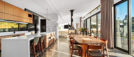 A modern kitchen with a central island, a dining area with a large table, and a view of the outdoors through large windows.