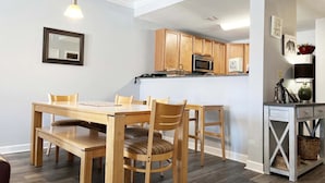 Un comedor con mesa y sillas de madera, una cocina con armarios de madera y una pequeña consola con cestas.