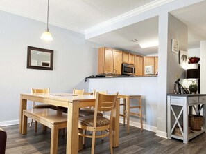 Un comedor con mesa y sillas de madera, una cocina con armarios de madera y una pequeña consola con cestas.