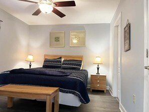 Un dormitorio con cama, mesitas de noche, ventilador de techo y decoración en la pared.
