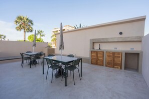 An outdoor patio with a table and chairs, a grill, and a wall with wooden cabinets. - Casa Revo - Pool, 5BR, Steps from the beach (La Paz)