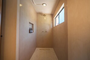A narrow, well-lit walk-in shower with a small shelf holding toiletries, a ceiling light, and a window providing natural light. - Casa Revo - Pool, 5BR, Steps from the beach (La Paz)