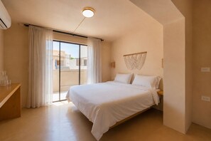 A bedroom with a bed, a wooden nightstand, a wall-mounted light fixture, and a view through a sliding glass door. - Casa Revo - Pool, 5BR, Steps from the beach (La Paz)