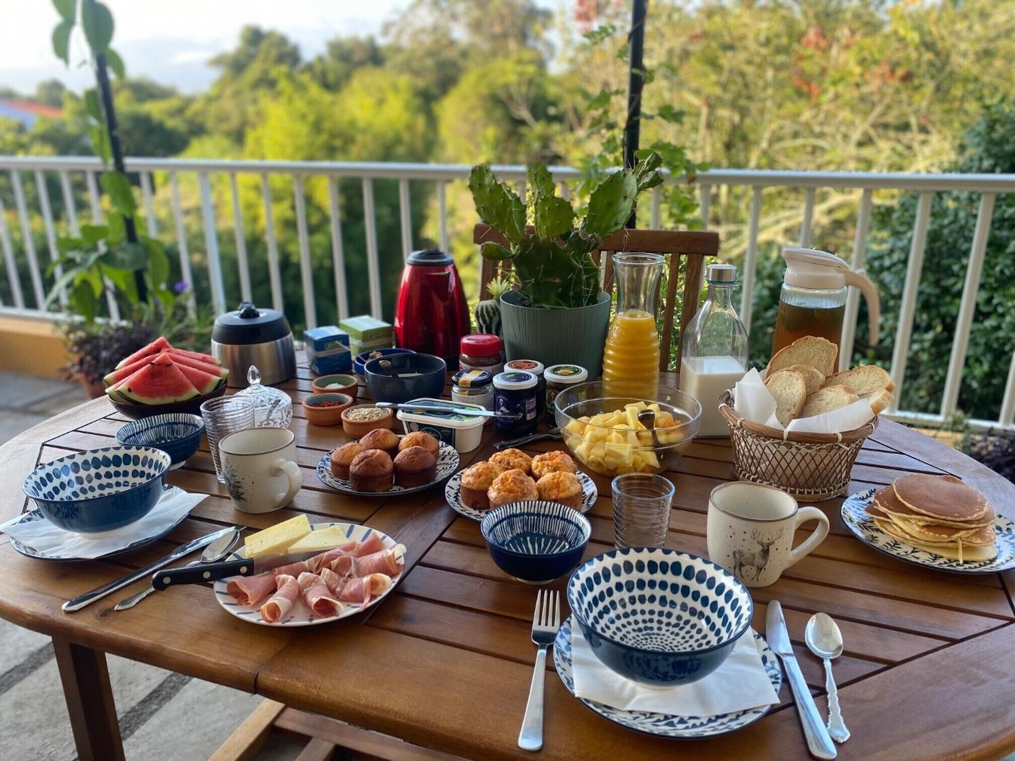 A breakfast table with various food items, utensils, and a potted plant.