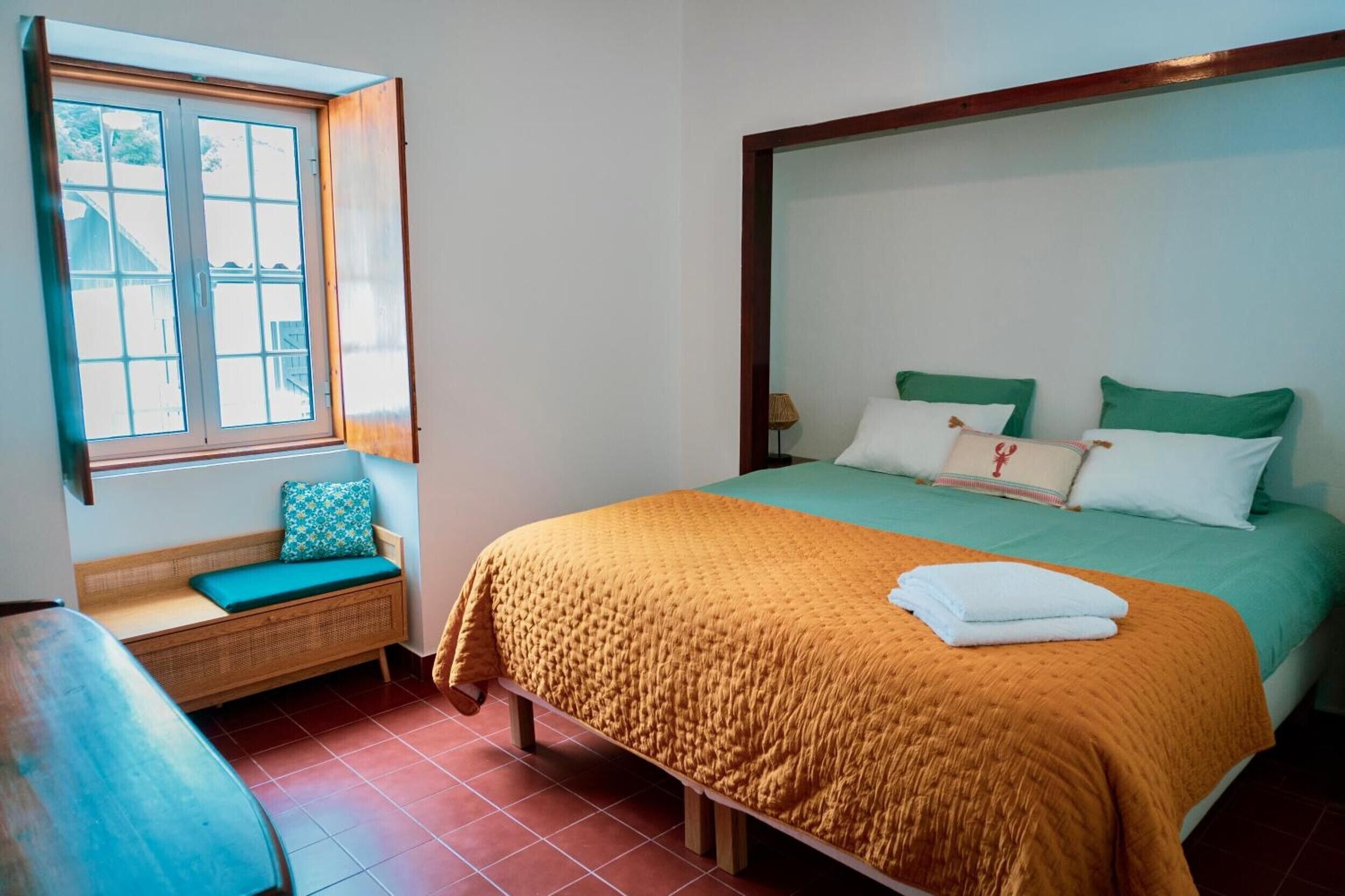 A bedroom with a bed, pillows, a window, and a bench.
