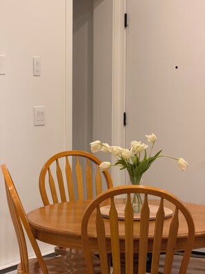 Et spiseområde med et træbord og stole, en vase med hvide blomster, og en hvid dør med sort greb.
