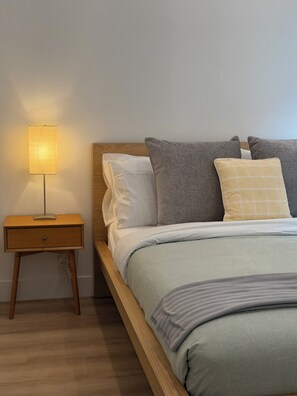 En pænt redt seng med et træsengegærde, et sengebord med en lampe, og en enkel væg.