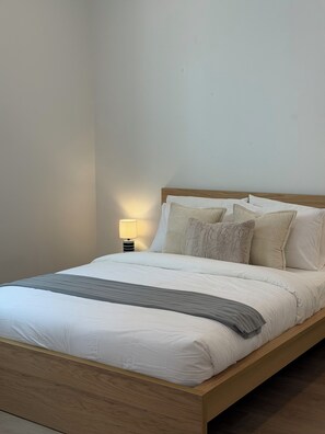 Ein ordentlich bezogenes Bett mit Holzbettgestell, weißer Bettwäsche und einer Nachttischlampe.