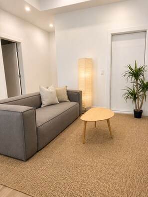 En moderne stue med en gr å sofa, et rundt træbord, en gulvlampe og en potteplante.