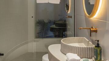 Un baño moderno con cabina de ducha de vidrio, un lavabo redondo con encimera color beige y un espejo grande con marco dorado.