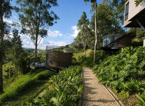 A modern house with a pathway leading to a balcony, surrounded by lush greenery and trees. - Hotel Velto Serene (El Peñol)
