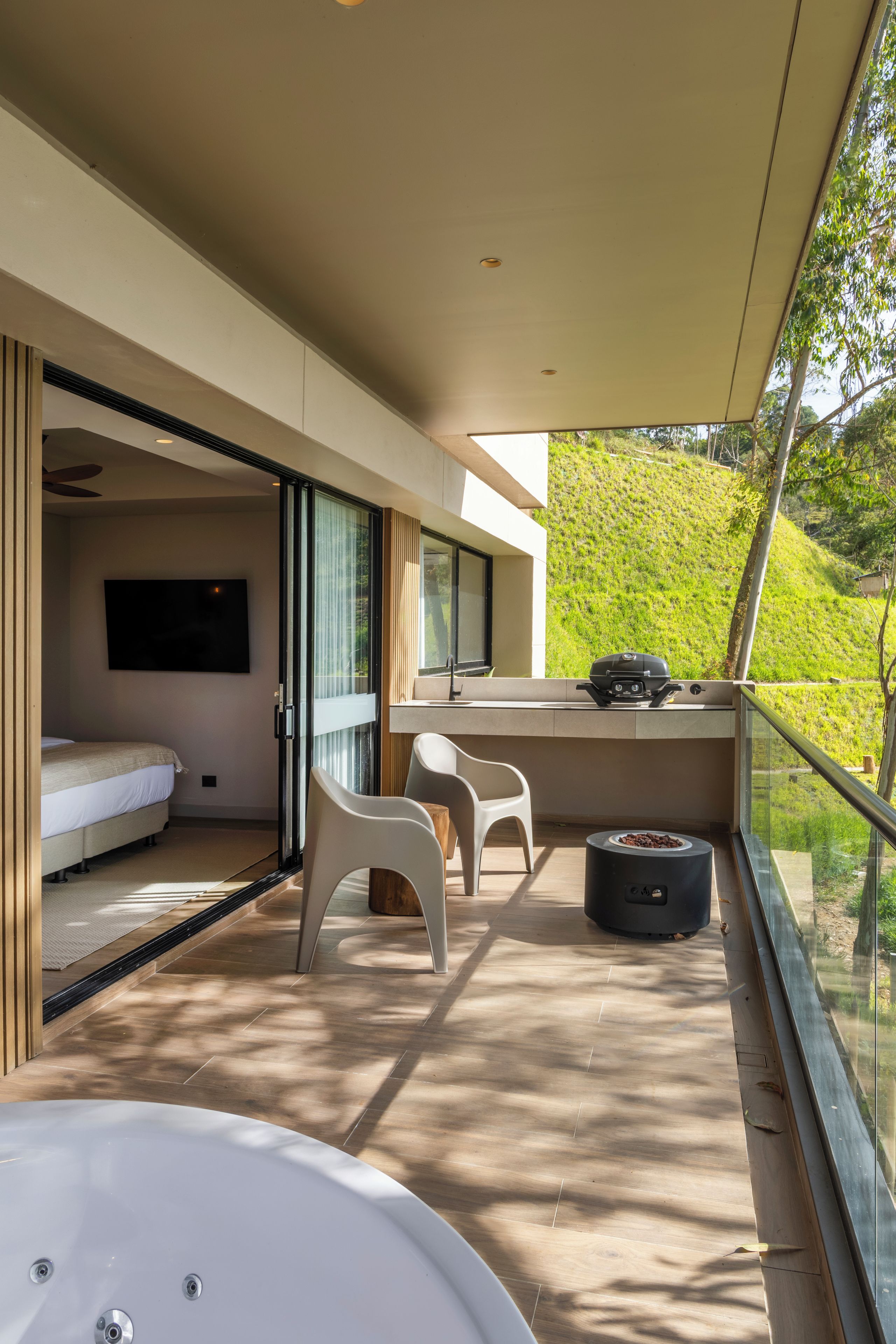 A modern balcony with a sofa, chairs, a dining table, and a grill.