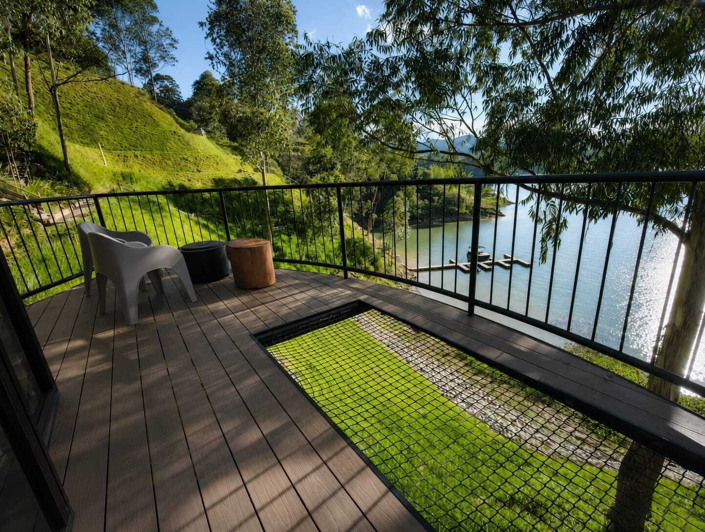 A deck with a view of a lake, a chair, a stool, and a small garden area.