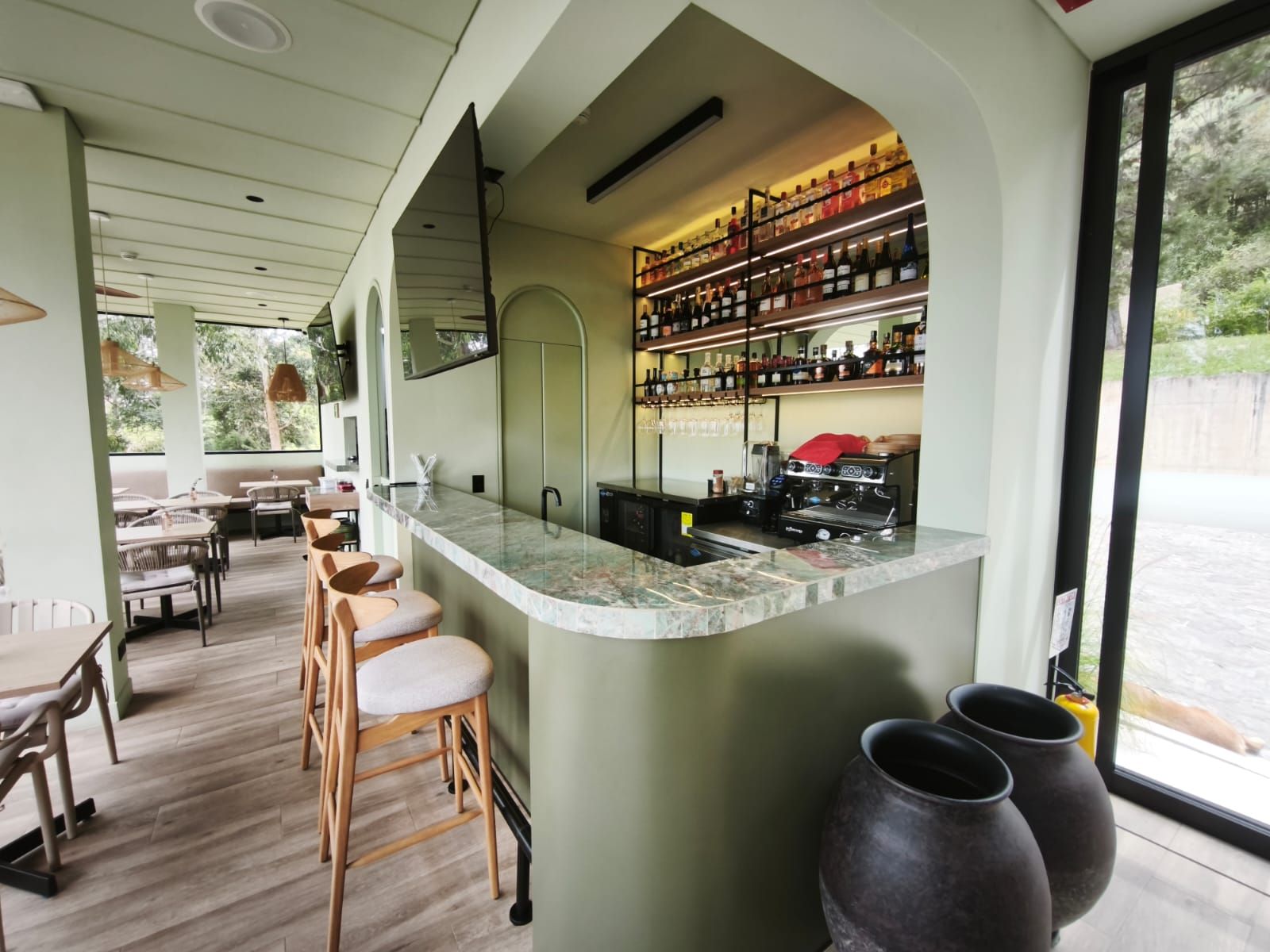 Una zona de bar con mostrador de mármol, taburetes de madera y una cafetera.