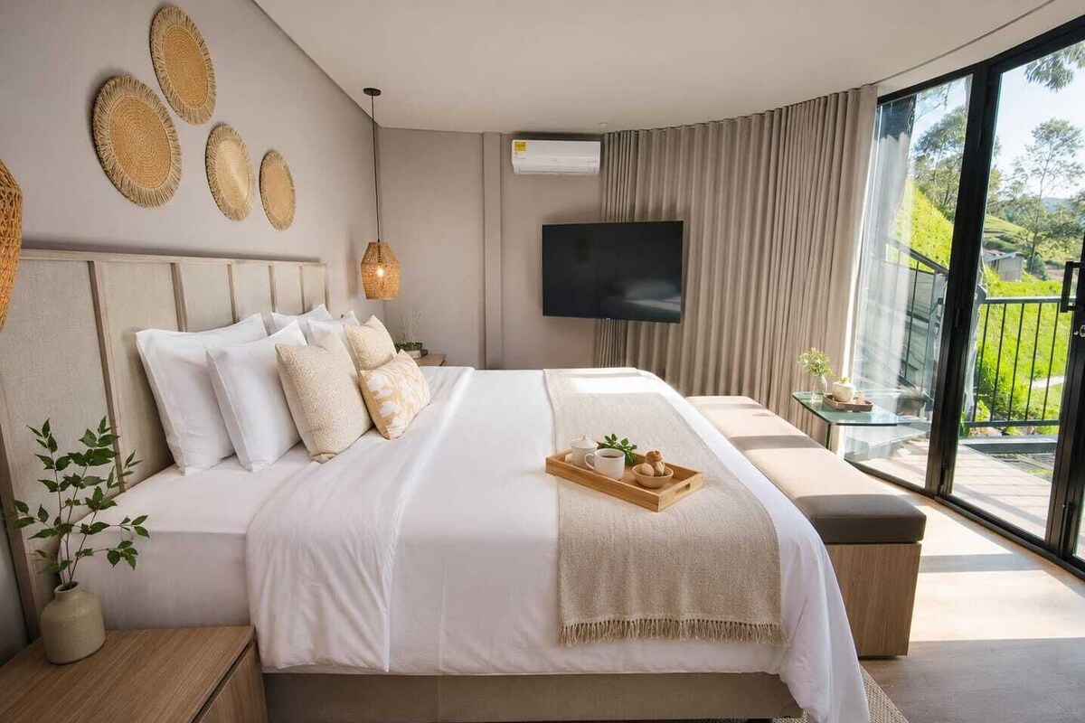 A modern bedroom with a large bed, a flat-screen TV, and a balcony with a view.