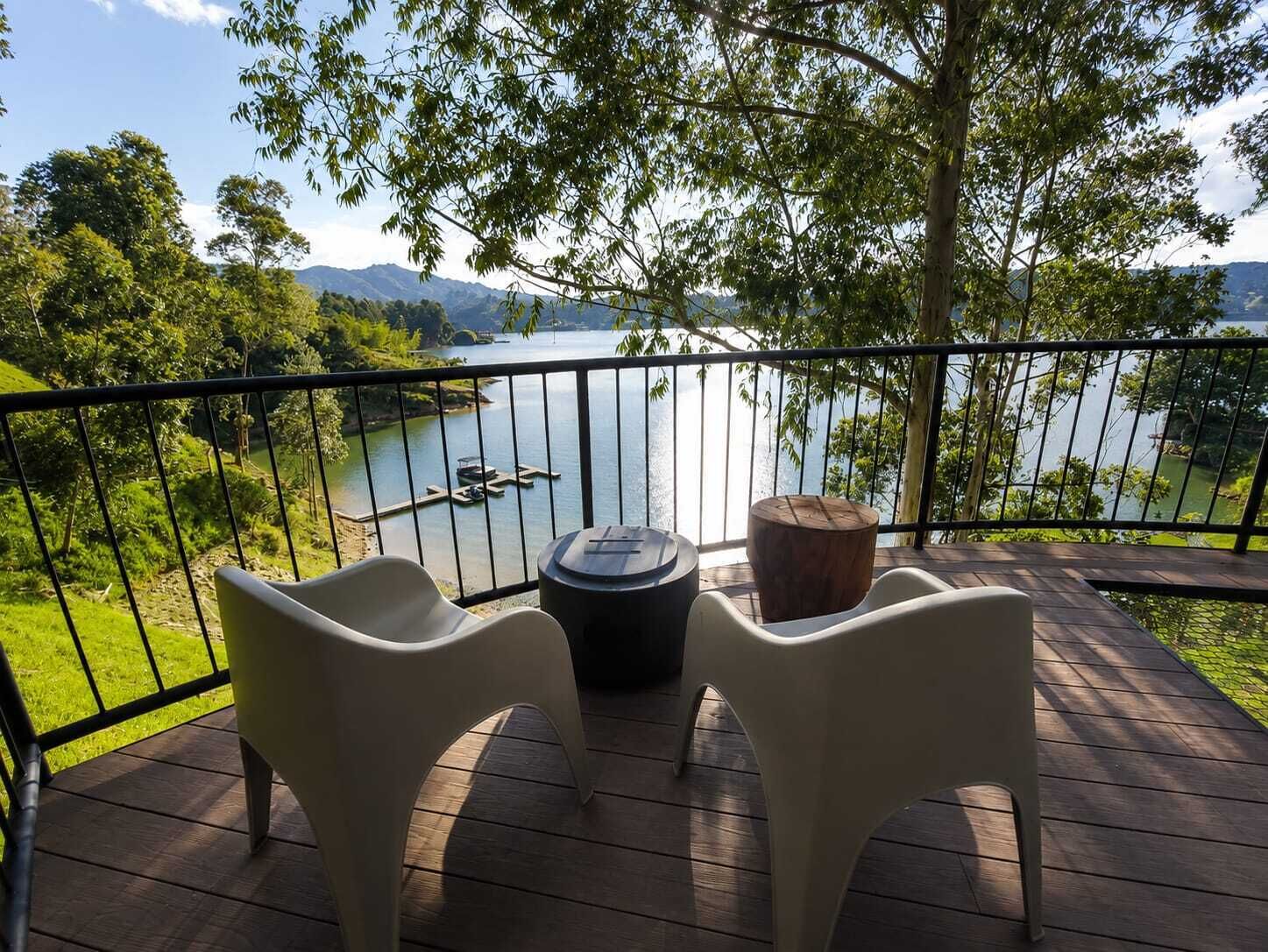 Terraza con dos sillas y una mesa, con vista a un lago con barcos y vegetación.