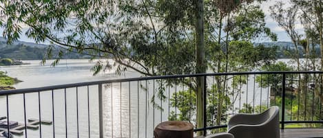A balcony with a view of a lake, a wooden table, and two chairs.