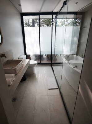 A modern bathroom with a glass shower enclosure, a bathtub, a toilet, and a vanity with a sink and towel storage. - Hotel Velto Serene (El Peñol)