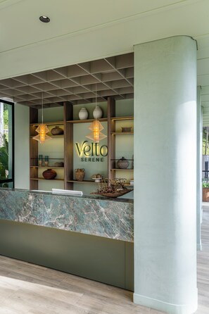 Un mostrador de recepción con encimera de mármol, estanterías con adornos y un letrero que dice 'Velto Serene'.