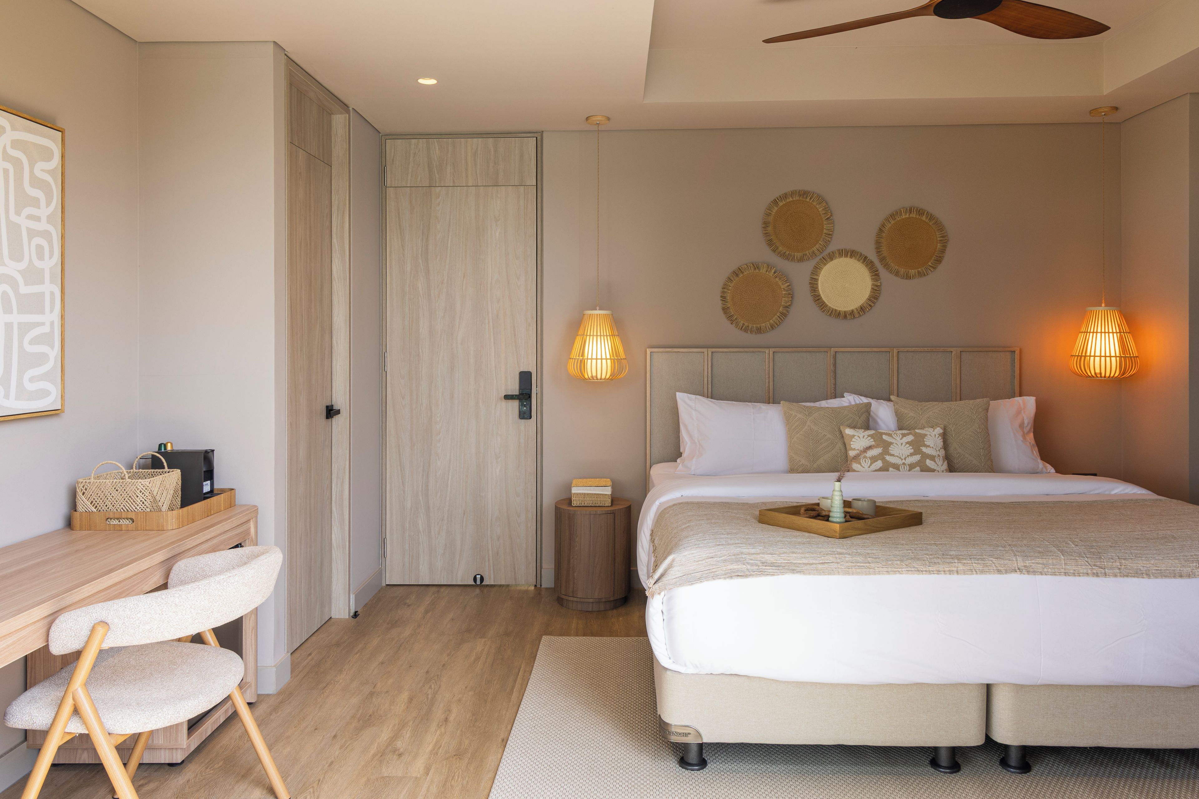 Un dormitorio con cama, mesita de noche, silla y escritorio con otra silla. Hay lámparas de pared y un ventilador de techo.