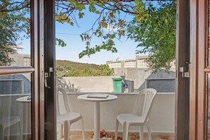 A balcony with two white plastic chairs, a small round table, and a view of a hillside. - Room 'Orama 25' with Sea View, Wi-Fi and Air Conditioning (Εύβοια)