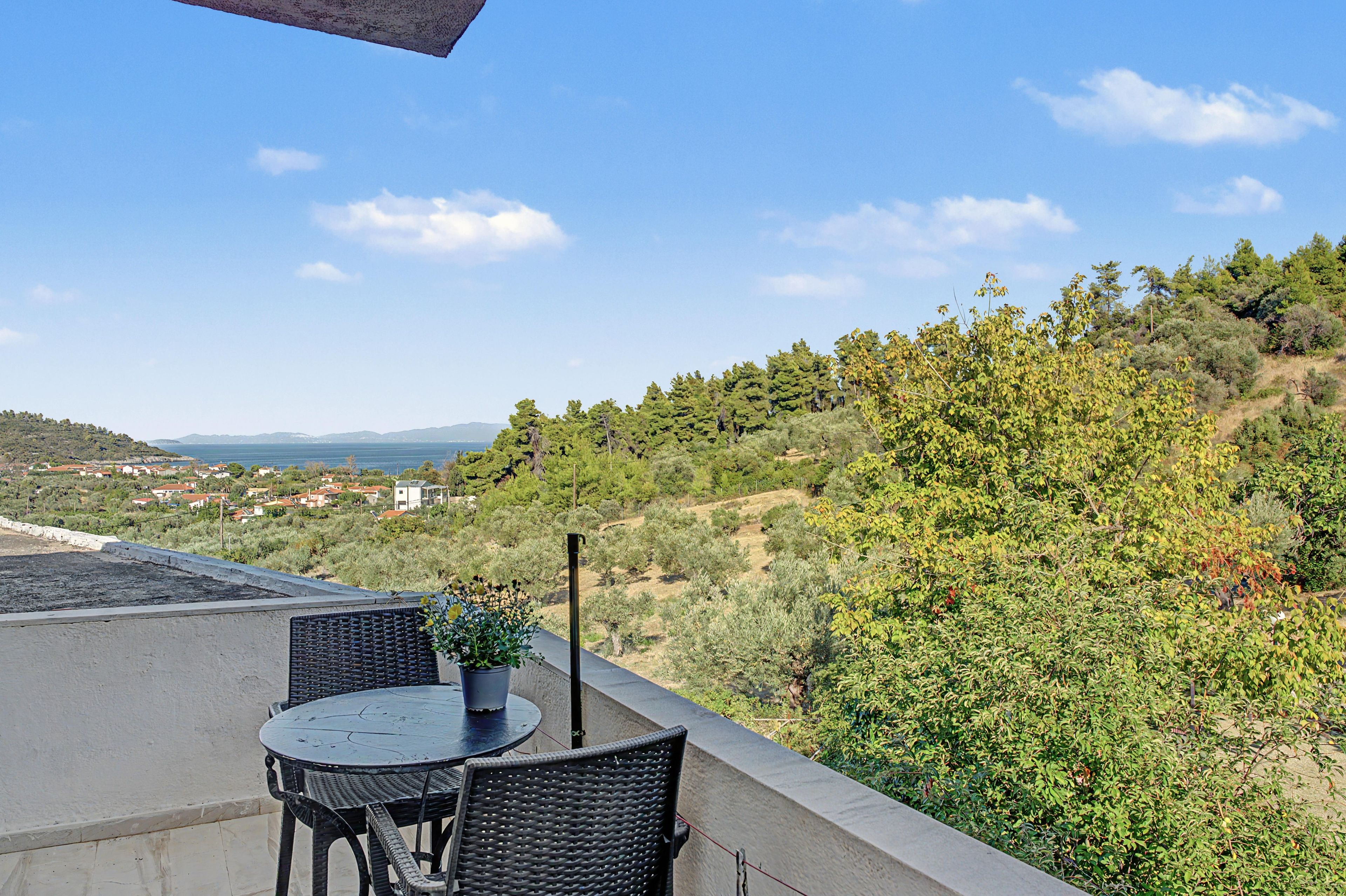 Eine Terrasse mit Tisch und Stühlen, die auf einen Hügel mit Bäumen und eine entfernte Ansicht von Häusern blickt.