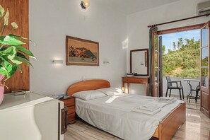Ein Schlafzimmer mit Bett, Nachttisch, einer Topfpflanze, einem Gemälde und Blick ins Freie.