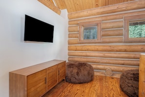 Ein Blockhaus-Interieur mit einem flachbildfernseher an der Wand, Holzbänken und einem großen Fenster mit Blick auf Bäume.