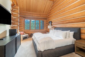 A log cabin bedroom with a bed, a TV, and a window with a view of trees. - Luxury Mountain Village Retreat | Panoramic Mountain Views | Private Hot Tub | Sleeps 9 (Telluride)